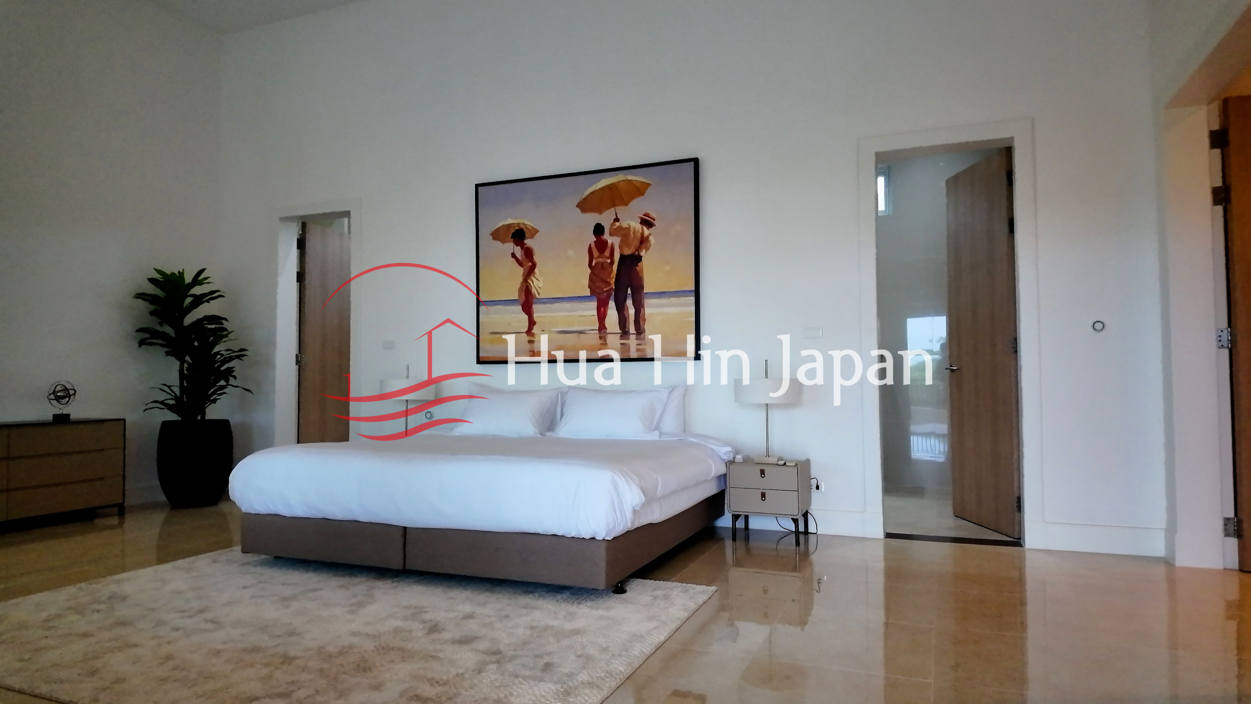 Elegant master bedroom with a large bed, white bedding, framed beach artwork, wooden flooring, and indoor plant